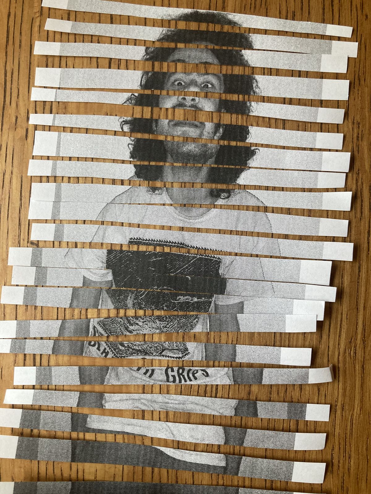 The same portrait cut into vertical strips before weaving, laid out in order on a wood table, showing the face and curly hair split into columns.