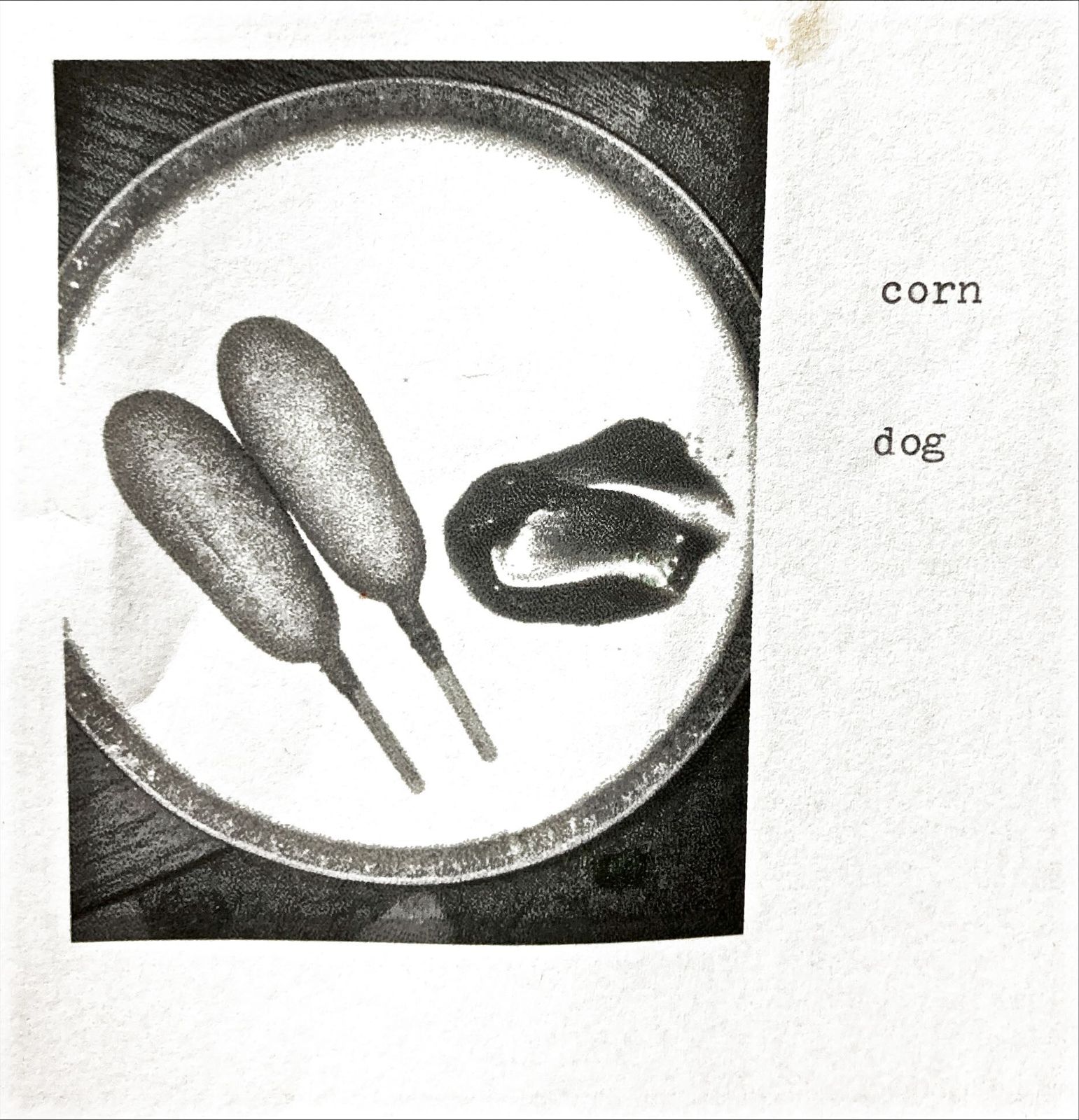 A halftone photocopy of two corn dogs and a bitten third one on a plate. Typewritten text alongside reads: corn dog.